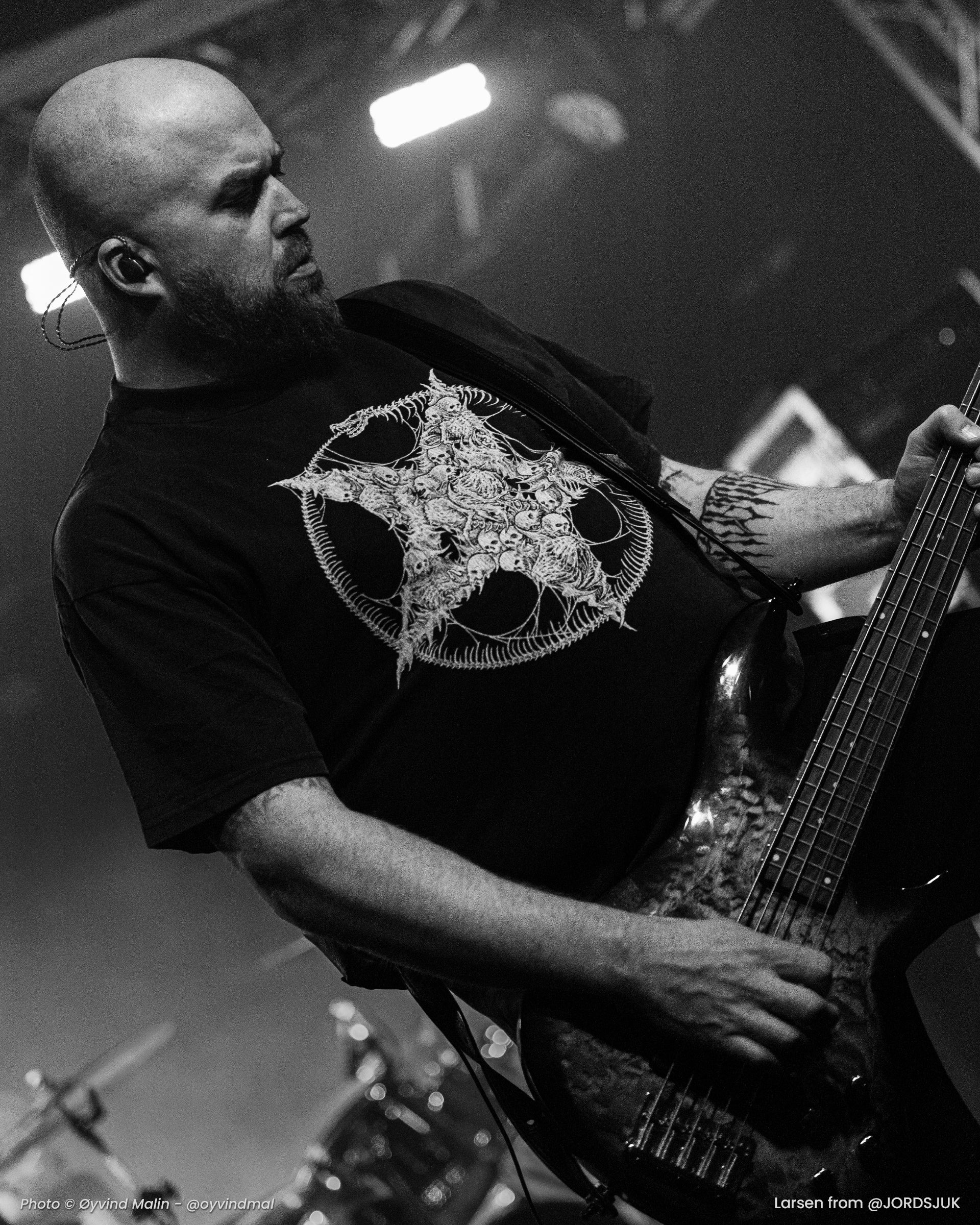 Man playing bass guitar on stage with a pentagram design on his t-shirt