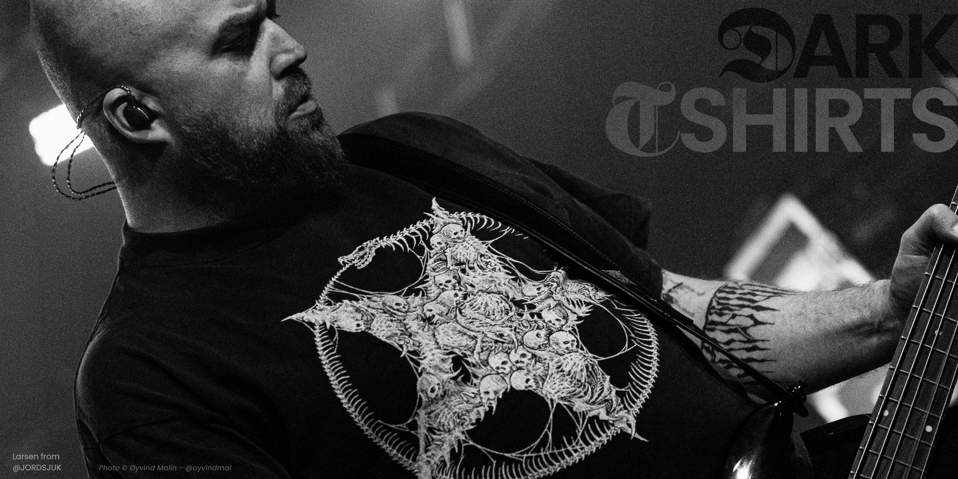 Person wearing a dark t-shirt with a white pentagram design, holding a bass guitar.