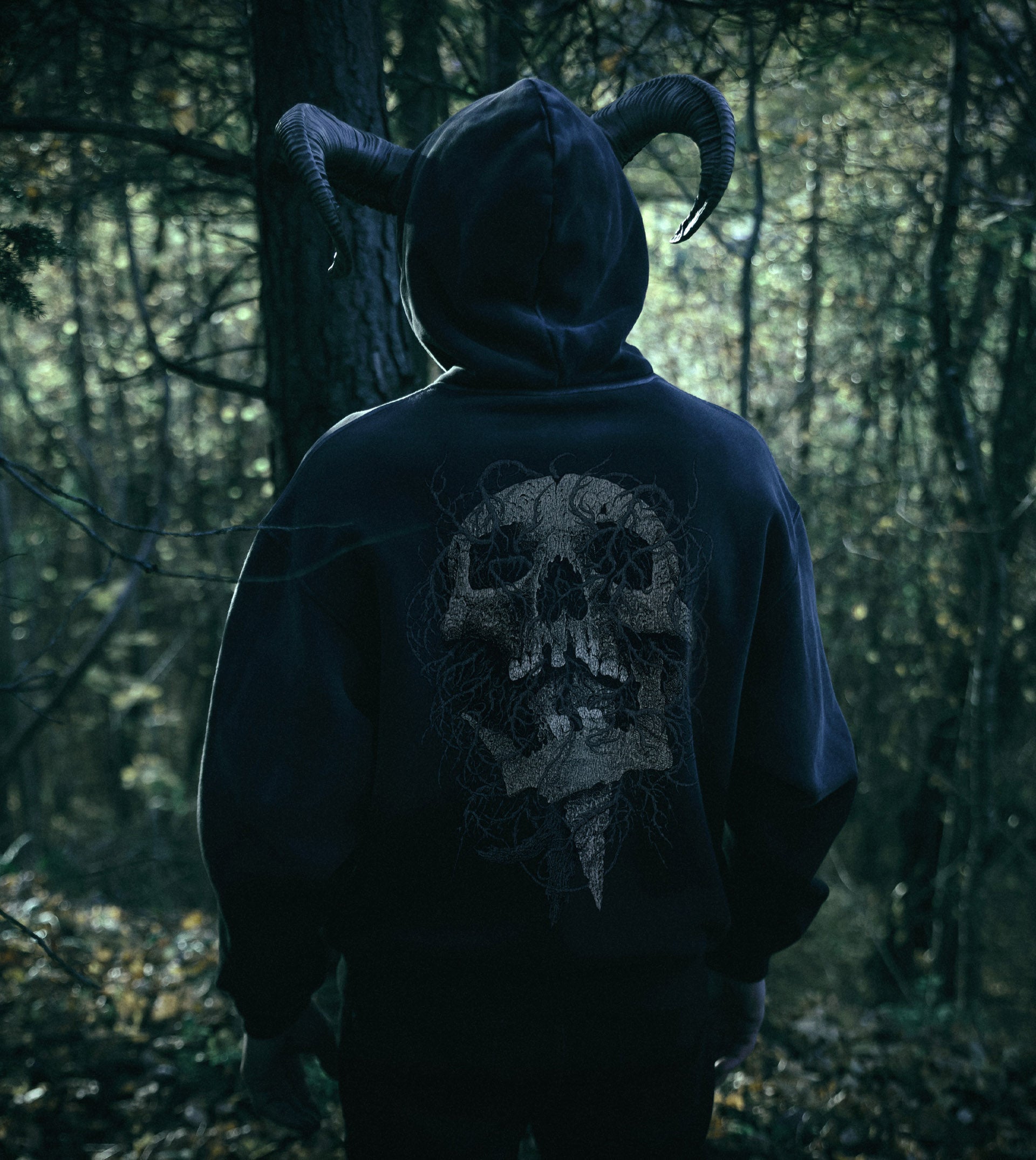 Person wearing a dark hoodie with a skull design in a forest setting