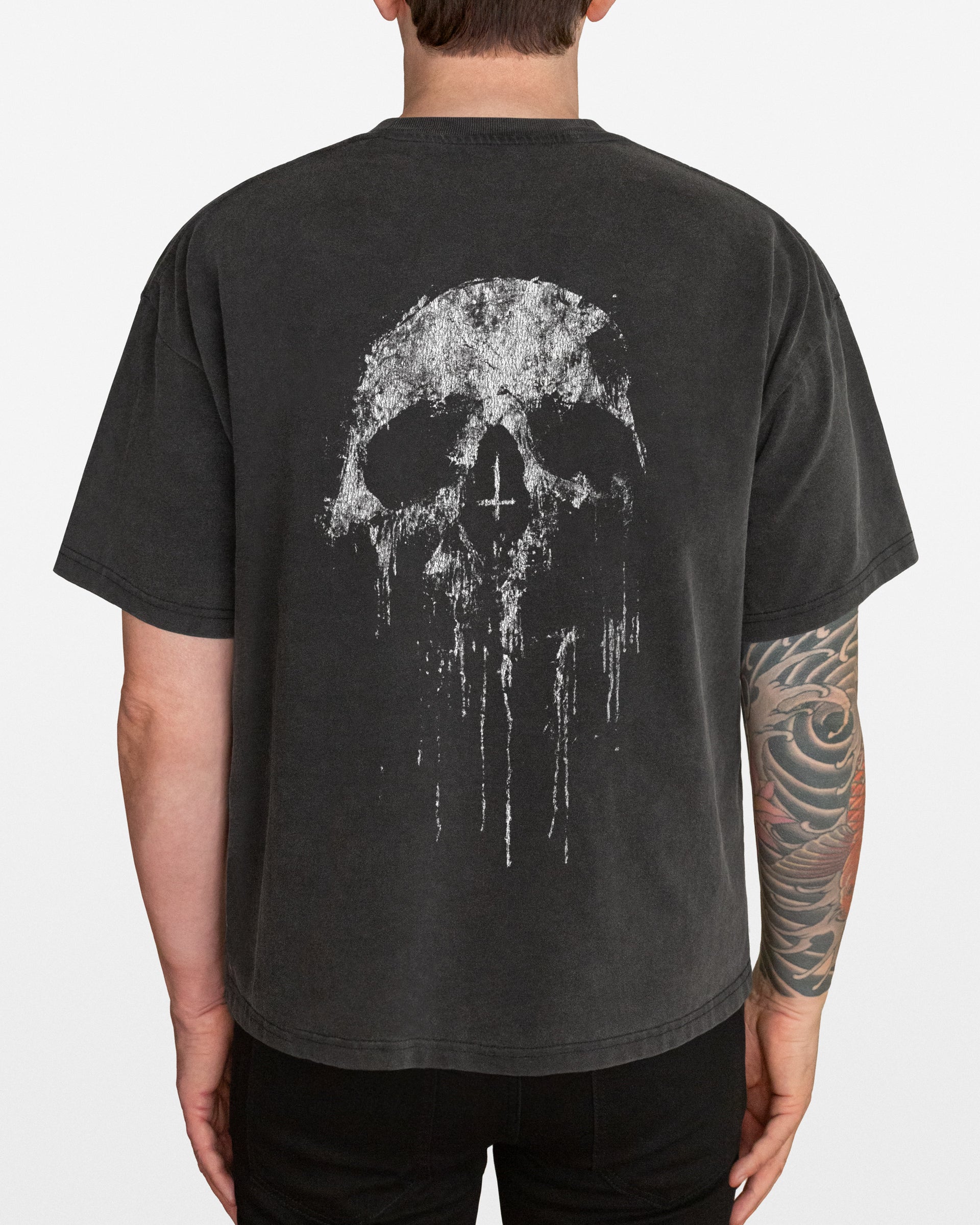 A dark gray acid wash oversized t-shirt with a distressed skull design on the back, worn by a person.