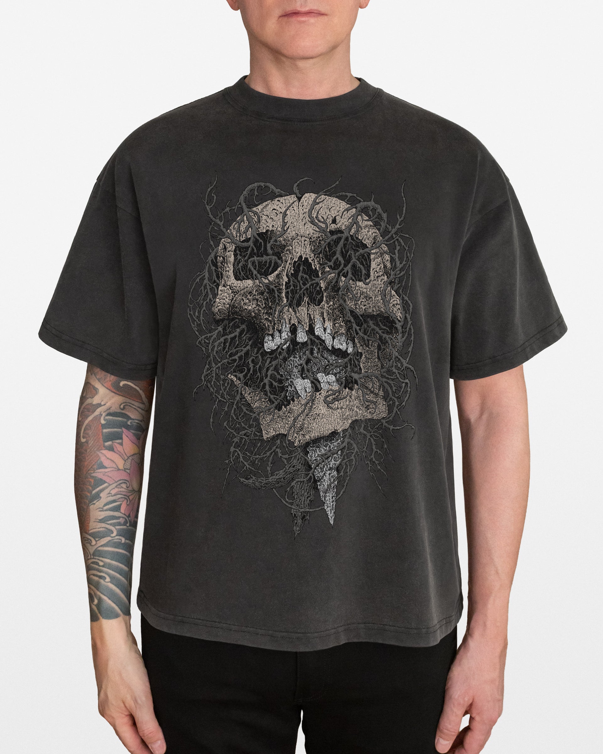 Person wearing a dark gray acid wash oversized t-shirt with an intricate skull design, on a white background