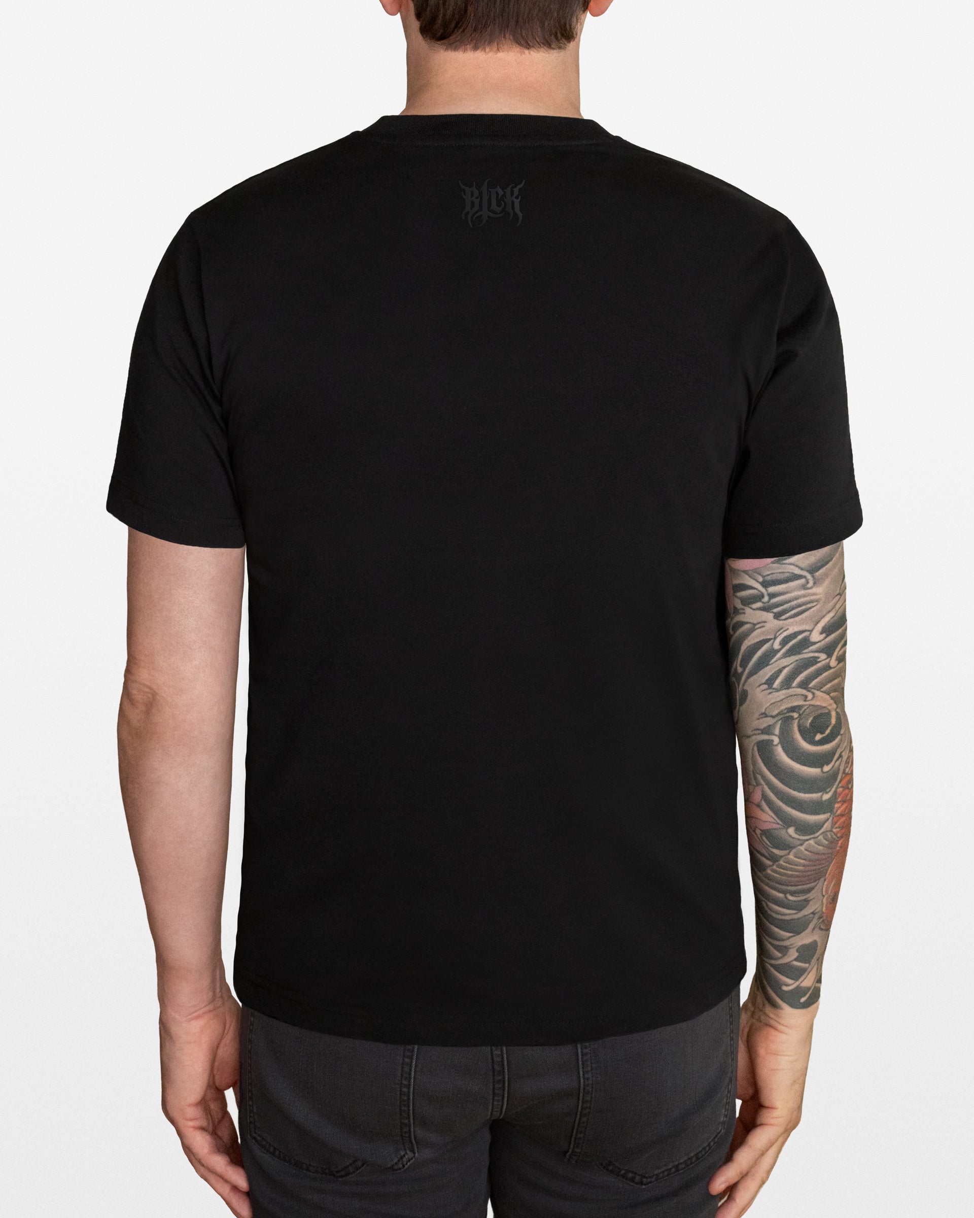 Person wearing a black t-shirt with a small BLCK logo on the back neck area, standing against a white background