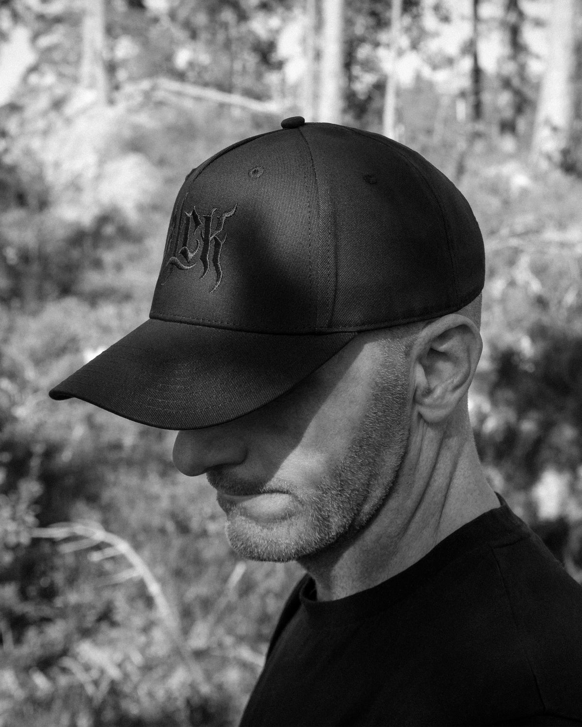 Person wearing a black cap with an embroidered BLCK logo, in a forest background