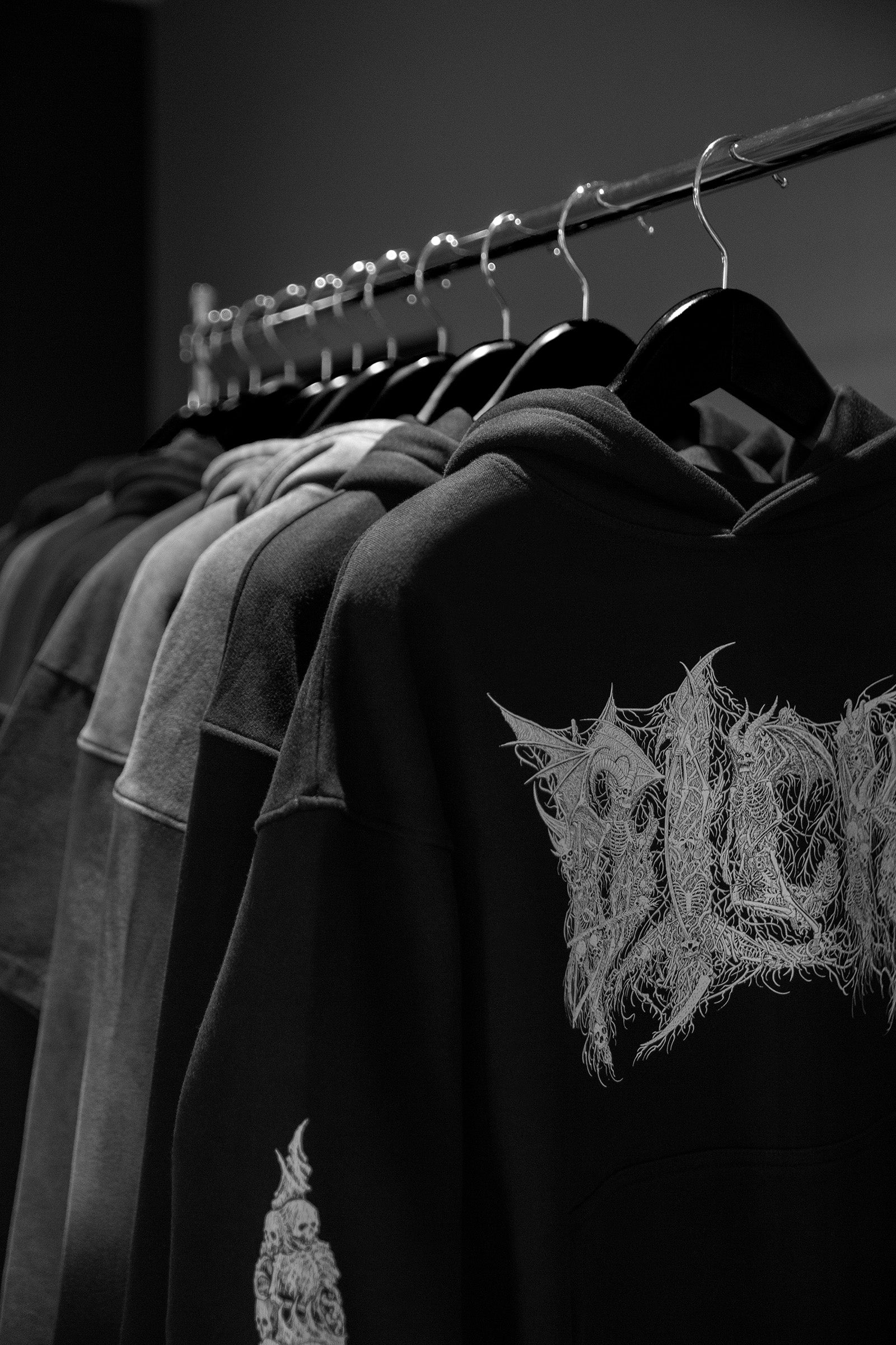 Clothing rack with hoodies, one featuring an illustrated logo, in a black and white setting.