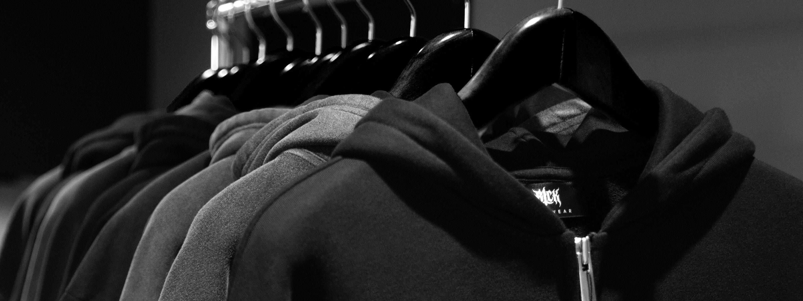 Row of dark hoodies on hangers against a neutral background