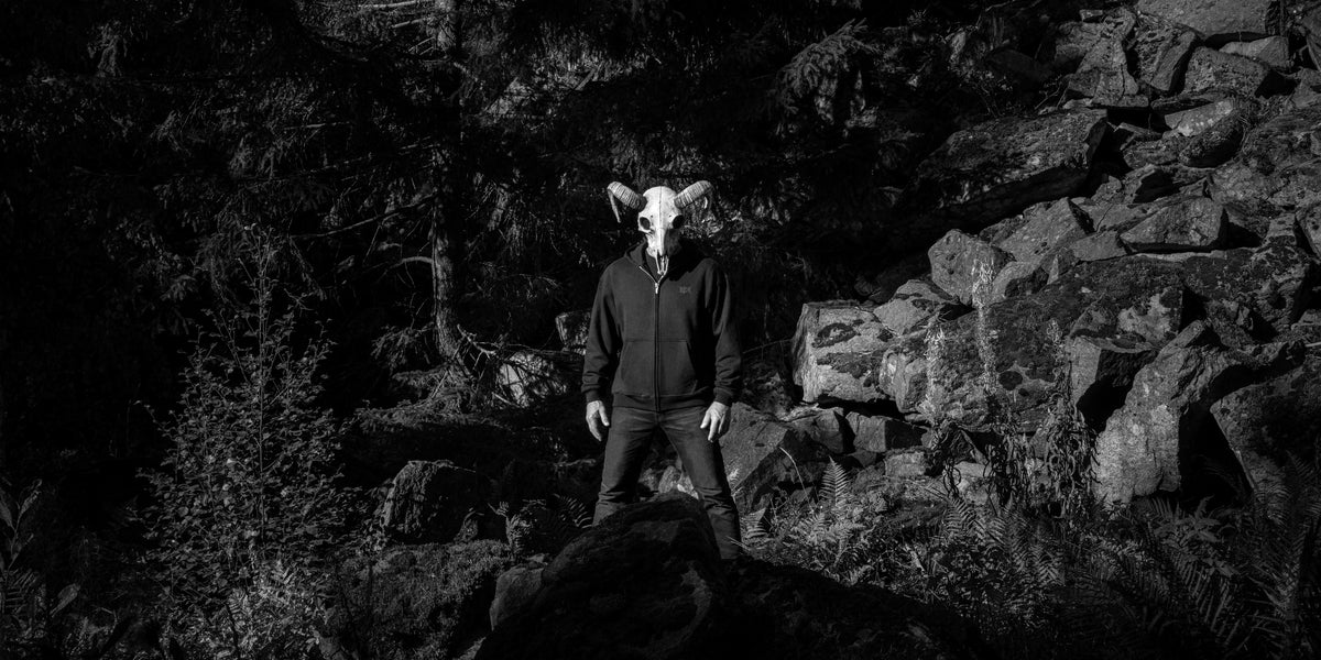 Person wearing a skull mask and a black hoodie, in a forest