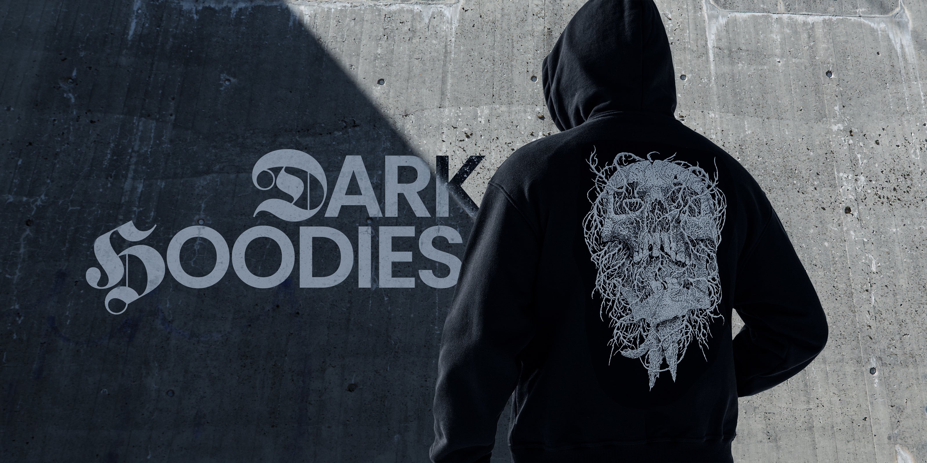 Person wearing a black hoodie with a skull design on the back, standing against a textured wall 