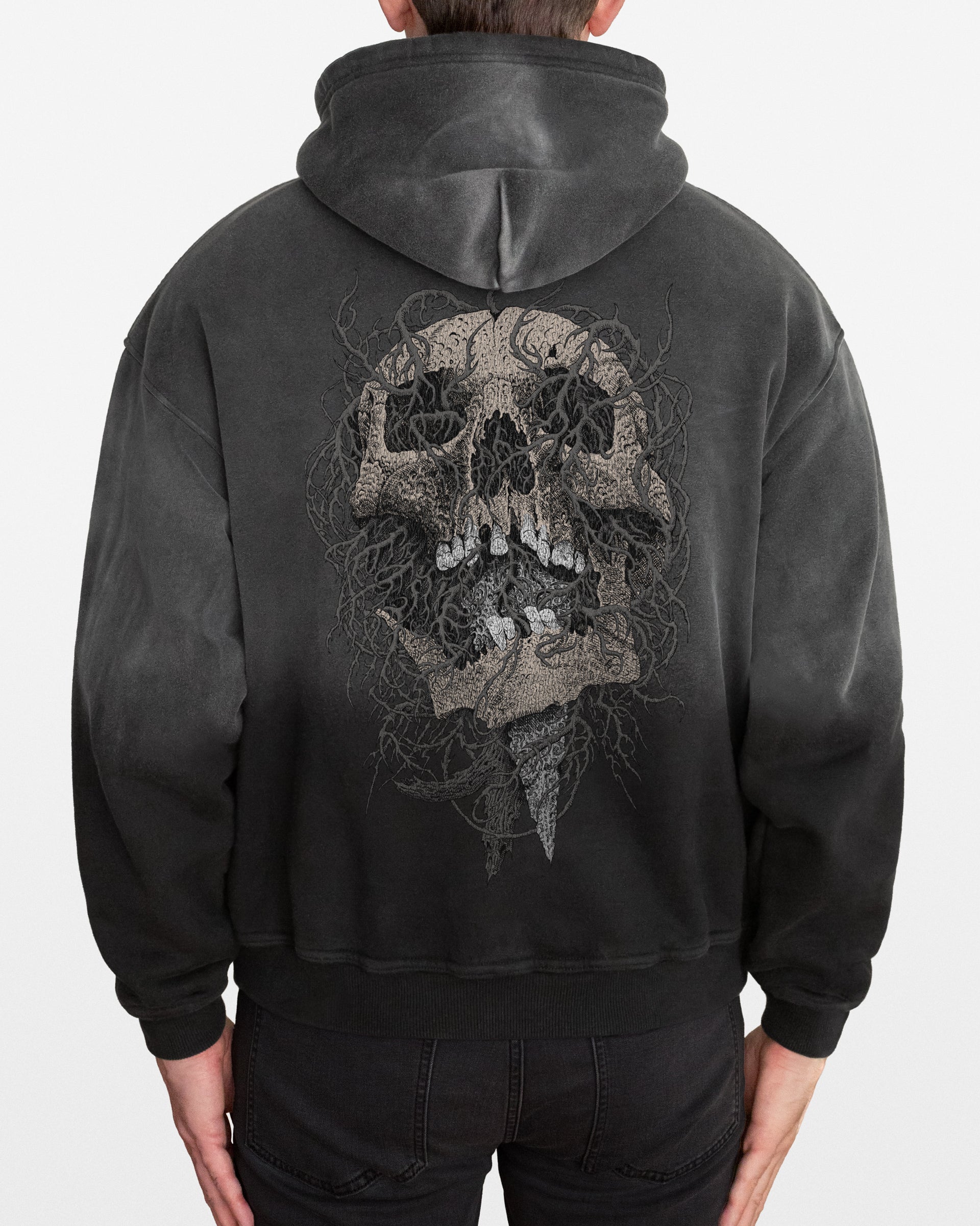 Dark gray sun faded hoodie with an intricate skull design on the back, worn by a person, on a white background