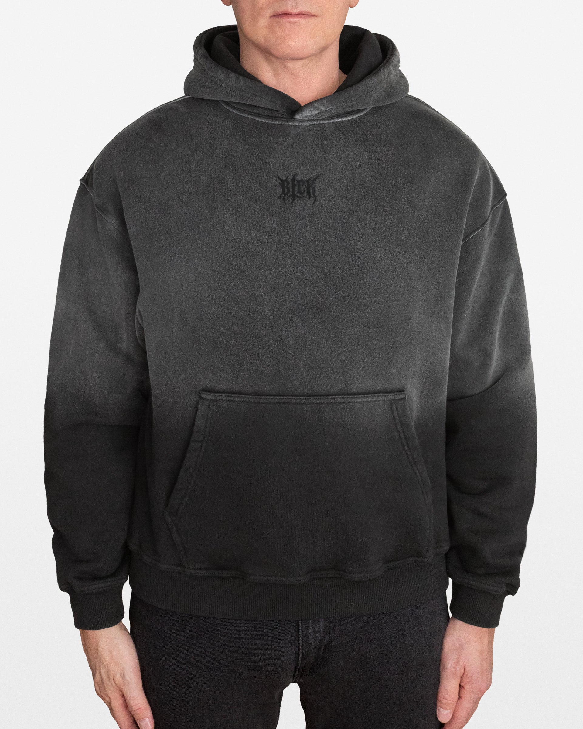 Person wearing a dark gray sun faded hoodie with a small BLCK  logo on the lefs side chest, on a white background