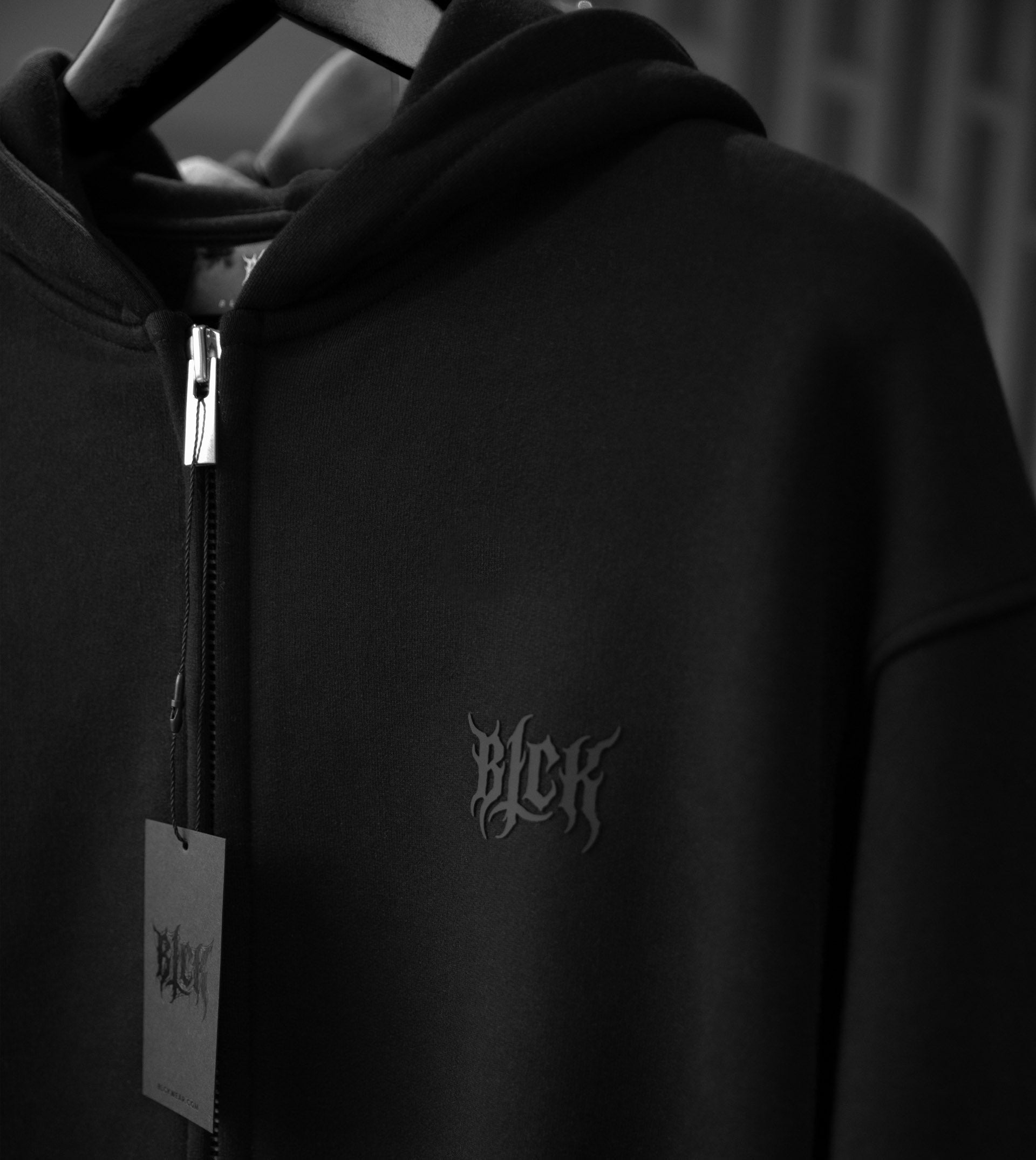 Black zip hoodie with a BLCK brand logo on a hanger against a blurred background