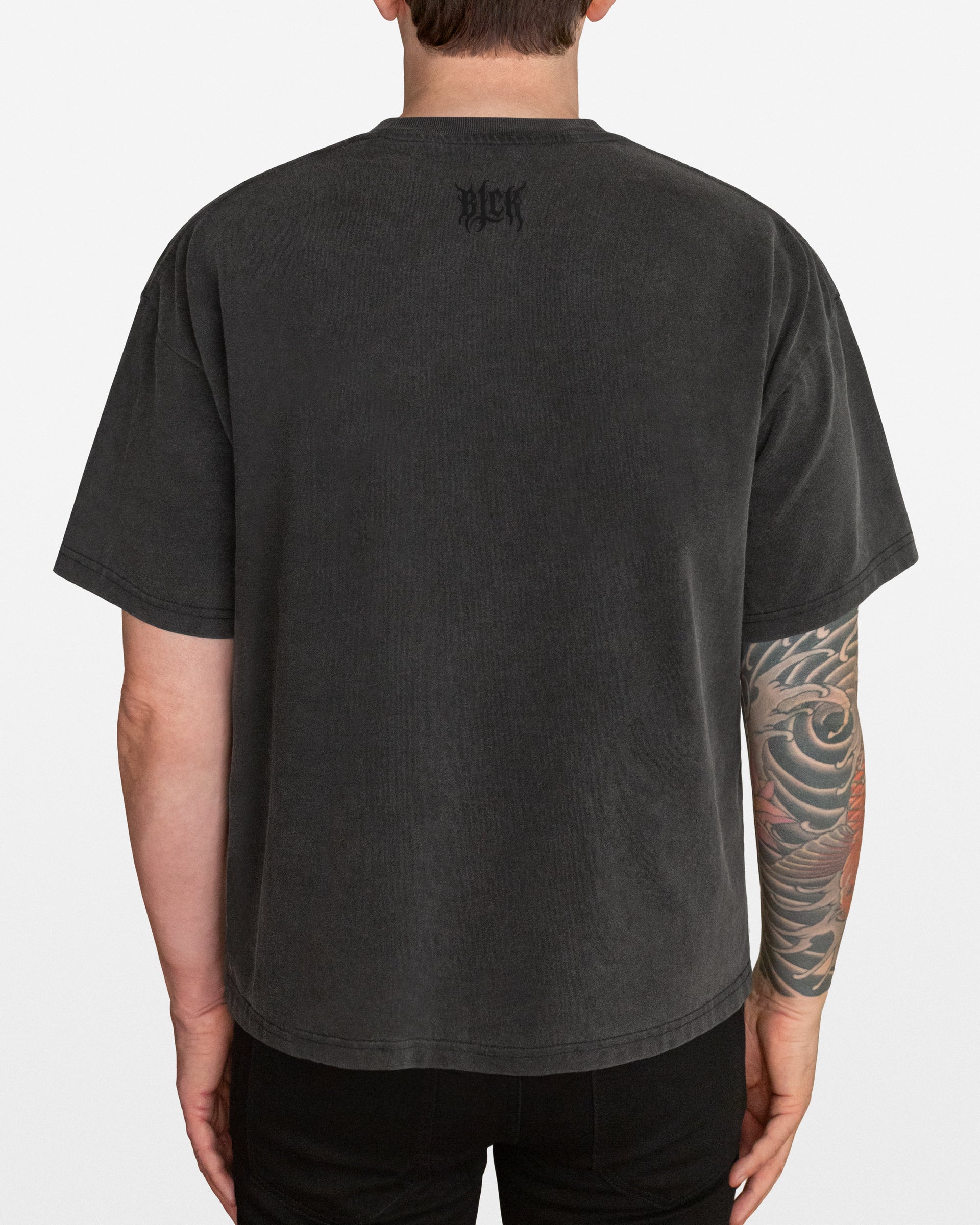 Person wearing a dark gray acid wash oversized t-shirt with a small BLCK logo by the neck, on a white background