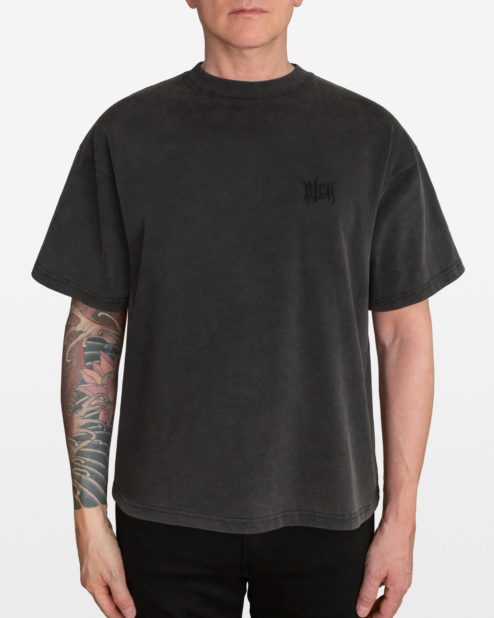 Person wearing a dark gray acid wash oversized t-shirt with a small BLCK logo on the left side chest, on a white background